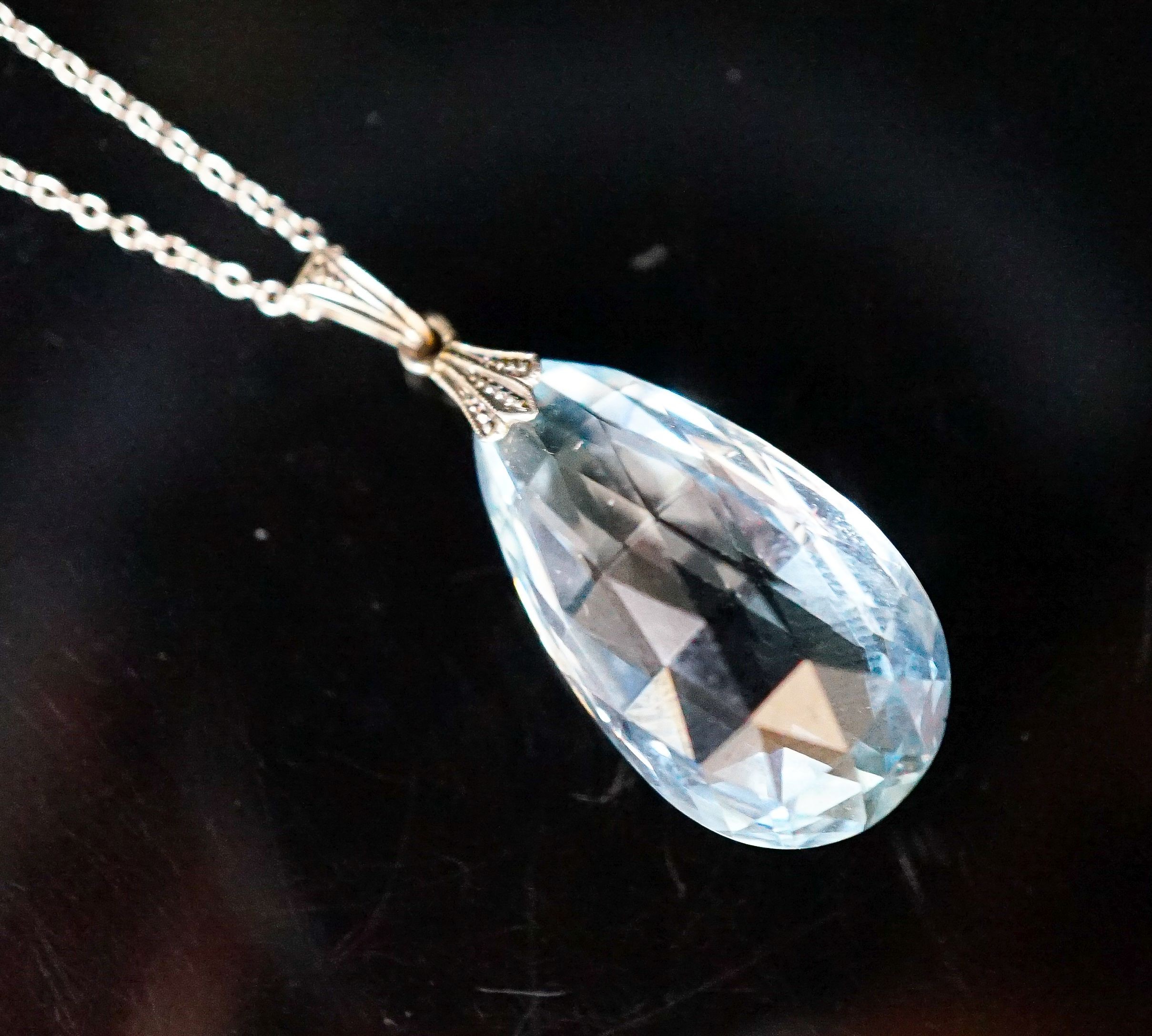 An 18ct mounted facetted pear cut aquamarine set pendant, 33mm, on a 375 white metal fine link chain, 45cm, gross weight 5.2 grams.